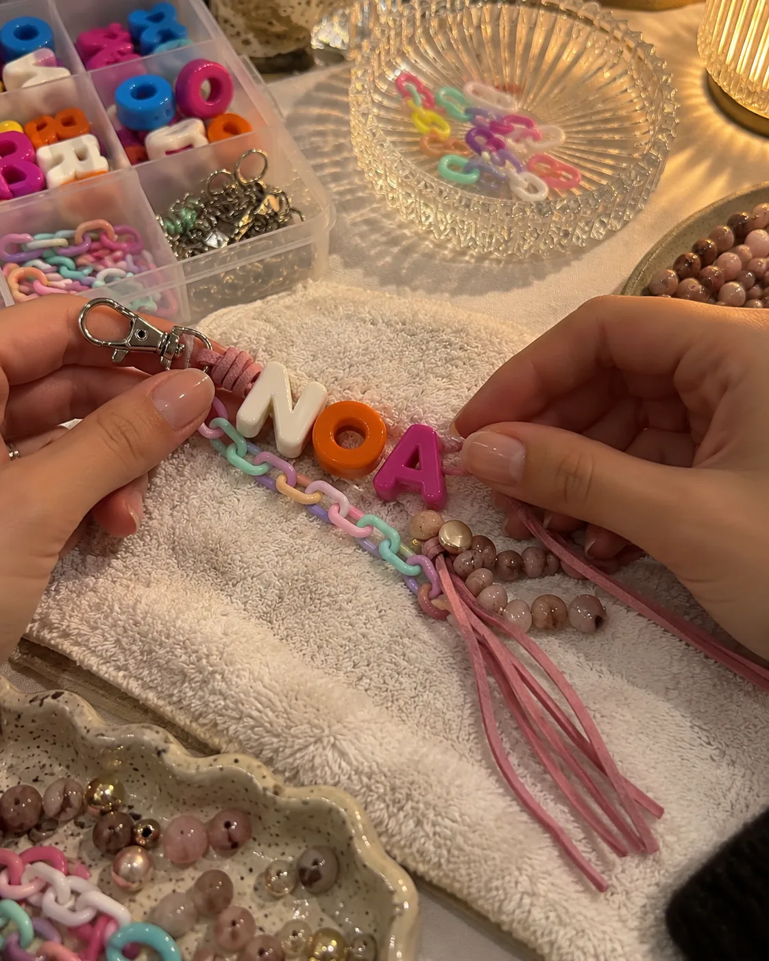 ידיים משחילות חרוזי אותיות למחזיק מפתחות עם השם NOA